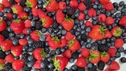 Verschiedene Beeren liegen gemischt auf einer wei&szlig;en Fl&auml;che: Erdbeeren, Blaubeeren, Brombeeren und Himbeeren.