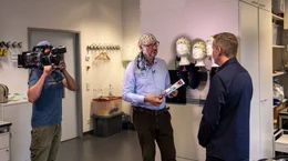 Leibniz-Institut f&uuml;r Neurobiologie Magdeburg: Vor der MDR-Kamera im Gespr&auml;ch: Eckart von Hirschhausen (Mitte) mit einer EEG-Haube und Informatiker Dr. Christoph Reichert. Er hat eine Methode entwickelt, die bald Locked-in-Patienten zugutekommen soll.