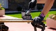 Eine Person mit Schutzhandschuhen reinigt ein metallisches Autoteil auf einer Werkbank im Freien. Eine Person mit Schutzhandschuhen reinigt ein metallisches Autoteil auf einer Werkbank im Freien.