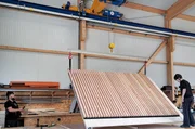 In der Werkhalle: Die Zimmerleute heben die fertige Seitenwand für den Carport mit einem Deckenkran an. In der Werkhalle: Die Zimmerleute heben die fertige Seitenwand für den Carport mit einem Deckenkran an.