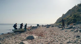 Leyla (Mala Emde, hinten links) und Tristan (Jonas Dassler, 3. von links) kommen auf der Insel an und werden von Stella (Edgar Selge, rechts) begr&uuml;&szlig;t. 2. von links: der Bootskapit&auml;n (Adam Bousdoukos).