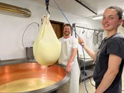 Senner Hannes Klingler und Praktikantin Jana heben K&auml;sebruch mit Tuch aus Kessel f&uuml;r Bergk&auml;seherstellung