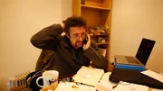 Richard sits in the workshop office on the phone, stressed.