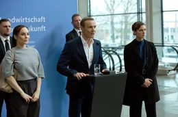 Wirtschafts- und Umweltminister Bauer (Mitte, Hannes Jaenicke) h&auml;lt eine umstrittene Rede, seine Personensch&uuml;tzerin Helen Schilling (r., Svenja Jung) und Staatssekret&auml;rin Dr. Karlstr&ouml;m (l.,Mina Tander) sind &uuml;ber die Reaktionen des Publikums besorgt.