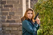 Marie (Katharina Wackernagel) duckt sich mit gezogener Waffe an die Kirchenmauer. Sie wartet auf den richtigen Moment f&uuml;r den Zugriff auf Gisela R&ouml;sler und Michelle Amsel.