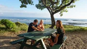 Home buyers Rachael Adair (M), Dan Adair (L) and Realtor Rebecca Morton (R) sitting at a picnic table by the ocean as seen on Hawaii Hunters (Action) Home buyers Rachael Adair (M), Dan Adair (L) and Realtor Rebecca Morton (R) sitting at a picnic table by the ocean as seen on Hawaii Hunters (Action)