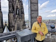 Wladimir Kaminer auf einer Aussichtsplattform des Kölner Doms mit Blick auf einen der Türme und die Stadt Köln im Hintergrund. Wladimir Kaminer auf einer Aussichtsplattform des Kölner Doms mit Blick auf einen der Türme und die Stadt Köln im Hintergrund.