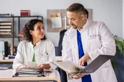 Dr. Leyla Sherbaz (Sanam Afrashteh, l.) und Dr. Matteo Moreau (Mike Adler, r.) schauen sich eine alte Notiz von Matteo an Leyla an, die sie an vergangene Zeiten als Kommilitonen erinnert.