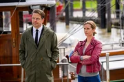Wolfgang Habedank (Holger Stockhaus) und Insa Scherzinger (Theresa Underberg) stehen vor einem Boot. Aus der Ferne unterhalten sie sich mit Yunus, der sich für Habedanks verschwundene Särge rechtfertigen soll. Wolfgang Habedank (Holger Stockhaus) und Insa Scherzinger (Theresa Underberg) stehen vor einem Boot. Aus der Ferne unterhalten sie sich mit Yunus, der sich für Habedanks verschwundene Särge rechtfertigen soll.
