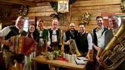 Moderatorin Conny B&uuml;rgler (2.v.l.) und Moderator Richard Deutinger (3.v.r.) posieren f&uuml;r ein Foto mit der Sch&ouml;nleitn Musi.