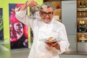 Starkoch Hans J&ouml;rg Bachmeier h&auml;lt einen L&ouml;ffel und ein Tellergericht in der Hand; Starkoch Hans J&ouml;rg Bachmeier best&auml;ubt einen Teller mit Pfannkuchen.