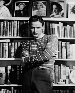 Schauspieler und Filmlegende Marlon Brando steht vor einem B&uuml;cherregal.