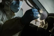 Eine Person in Schutzkleidung (PSA) entfernt Glassplitter vom Lenkrad des Autos. (Szene nachgestellt)