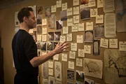 Tom Hiddleston betrachtet eine Pinnwand mit Hinweisen darauf, wie sich die Ereignisse in Pompeji nach dem Ausbruch des Vesuvs zugetragen haben.