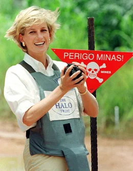 Prinzessin Diana l&auml;chelt neben einem Warnschild in einer Bombenweste.