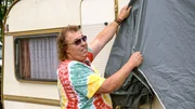 Der Mann nimmt die Abdeckung des Wohnmobils ab Der Mann nimmt die Abdeckung des Wohnmobils ab