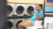 Rob sits on a washing machine in a laundromat while talking to his friends Ty and Tor'i.