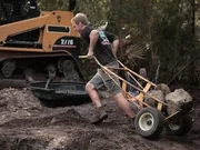Chris Hanson pulling a dolly full of stones at the Payne's house. Next the guys focus on the natural features of the pond, struggling to move a 10 foot long, 2,000 pound piece of Cypress tree into place, while dealing with placing thousands of pounds of Tennessee fieldstone.