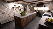 An after photo of the kitchen with the stairs in the background, as seen on Farmhouse Fixer, Season 3.
