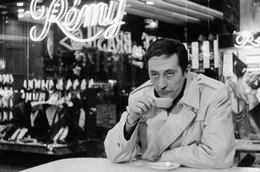 Jabeke (Jean Rochefort), in einen Trenchcoat gekleidet, beobachtet beim Kaffeetrinken die Szenerie.