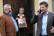 Zur Überraschung der Kommissare Stadler (Dieter Fischer, l.) und Hansen (Igor Jeftić, r.) zeigt Haushälterin Gerda Schlobinger (Johanna Bittenbinder, M.) ein Foto des wahren Pfarrers der Kirche Sankt Anian. Mit wem haben es die Kommissare im Fall des ermordeten Pfarrers tatsächlich zu tun? Zur Überraschung der Kommissare Stadler (Dieter Fischer, l.) und Hansen (Igor Jeftić, r.) zeigt Haushälterin Gerda Schlobinger (Johanna Bittenbinder, M.) ein Foto des wahren Pfarrers der Kirche Sankt Anian. Mit wem haben es die Kommissare im Fall des ermordeten Pfarrers tatsächlich zu tun?
