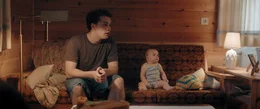 Rafael (Anselm Bresgott) und Baby Olivia (Patricia Graf) sitzen auf dem Sofa.