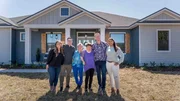 Homeowners Mirabel and Dustin smiling with hosts Brian and Mika Kleinschmidt and their family Rosie and Tita outside their brand new dream home on reveal day as seen on 100 Day Dream Home.
