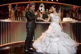 Moderator Caesar Flickerman (Stanley Tucci, l.) ahnt nicht, dass sich unter Katniss' (Jennifer Lawrence, r.) Brautkleid, das sie auf Snows Befehl hin tr&auml;gt, ein schwarzes Spottt&ouml;lpel-Kost&uuml;m versteckt ...