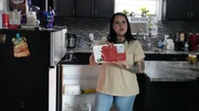 Wendy h&auml;lt Fleisch neben dem K&uuml;hlschrank in der Hand