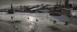 Eine verschneite Ortschaft. Jugendliche und Kinder spielen im Schnee und auf dem Eis.