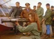 Capt. Santina (Jenny Gago, vorne), die Anführerin der Freiheitskämpfer, prüft ein Raketenabschussgerät. MacGyver (Richard Dean Anderson, l.) und Dalton (Bruce McGill, 2.v.l.) beobachten die heikle Situation. Capt. Santina (Jenny Gago, vorne), die Anführerin der Freiheitskämpfer, prüft ein Raketenabschussgerät. MacGyver (Richard Dean Anderson, l.) und Dalton (Bruce McGill, 2.v.l.) beobachten die heikle Situation.