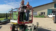 Obstbauer Wolfgang und Lena fahren auf einem Erntefahrzeug zur Apfelplantage.