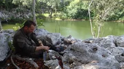 John Hudson sits on bank rocks in the shade of jungle trees while purifying water. John Hudson sits on bank rocks in the shade of jungle trees while purifying water.