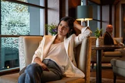 Bel Richmond (Rakhee Thakrar) hat mit ihrem Podcast zum Fall Rosie Duff zur Wiederaufnahme der Ermittlungen beigetragen. DS Karen Pirie (nicht im Bild) und ihr Kollege DS Phil Parhatka (nicht im Bild) befragen in einem schicken Hotel die Podcasterin Bel Richmond (Rakhee Thakrar), die eigene Recherchen zum Fall Rosie Duff durchgef&uuml;hrt hat.
