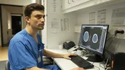 Rostock: young physician Max is sitting at a desk while giving an interview and explaining what he sees on the CT images of a skull on his computer screen. He is seemingly looking at the interviewer, while his hands are on the keyboard and the computer mouse. Rostock: young physician Max is sitting at a desk while giving an interview and explaining what he sees on the CT images of a skull on his computer screen. He is seemingly looking at the interviewer, while his hands are on the keyboard and the computer mouse.