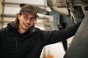 Medium-close up of Parker smiling and leaning against the plane - inside.