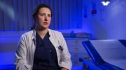 Lübeck: Assistant Surgeon Olga gibt ein Interview am Interview-Set. Sie trägt dunkelblaue OP-Kleidung und einen weißen Kittel; links von ihr befindet sich eine blaue, mit einem Papierlaken bedeckte Matratze. In ihrer Tasche sind unter anderem Scheren zu sehen. Lübeck: Assistant Surgeon Olga gibt ein Interview am Interview-Set. Sie trägt dunkelblaue OP-Kleidung und einen weißen Kittel; links von ihr befindet sich eine blaue, mit einem Papierlaken bedeckte Matratze. In ihrer Tasche sind unter anderem Scheren zu sehen.