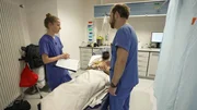Saarbrücken: one young doctor and another male physician both in blue scrubs are standing around a pixelated laying patient. The young doctor is intently listening to what her colleague says. To the right we see blue curtains, and in the back some light grey cabinets. Saarbrücken: one young doctor and another male physician both in blue scrubs are standing around a pixelated laying patient. The young doctor is intently listening to what her colleague says. To the right we see blue curtains, and in the back some light grey cabinets.