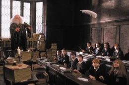 Professor Flitwick (Warwick Davis, l.) unterrichtet schon seit 40 Jahren in Hogwarts. Er lehrt Zauberkunst und ist so klein, dass er sich auf einen B&uuml;cherstapel stellen muss, um &uuml;ber das Lehrerpult schauen zu k&ouml;nnen. Interessiert verfolgen die Sch&uuml;ler den Zaubertricks.