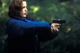 Scully (Gillian Anderson) zielt auf einen unsichtbaren Gegner, den sie zun&auml;chst f&uuml;r ein Raubtier hielt.