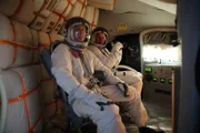 Two cosmonauts sit strapped into their seats.