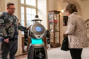 Ein Roboter steht zwischen Howard (Michael Cyril Creighton) und Meckertante Uma Heller (Jackie Hoffman) Ein Roboter steht zwischen Howard (Michael Cyril Creighton) und Meckertante Uma Heller (Jackie Hoffman)